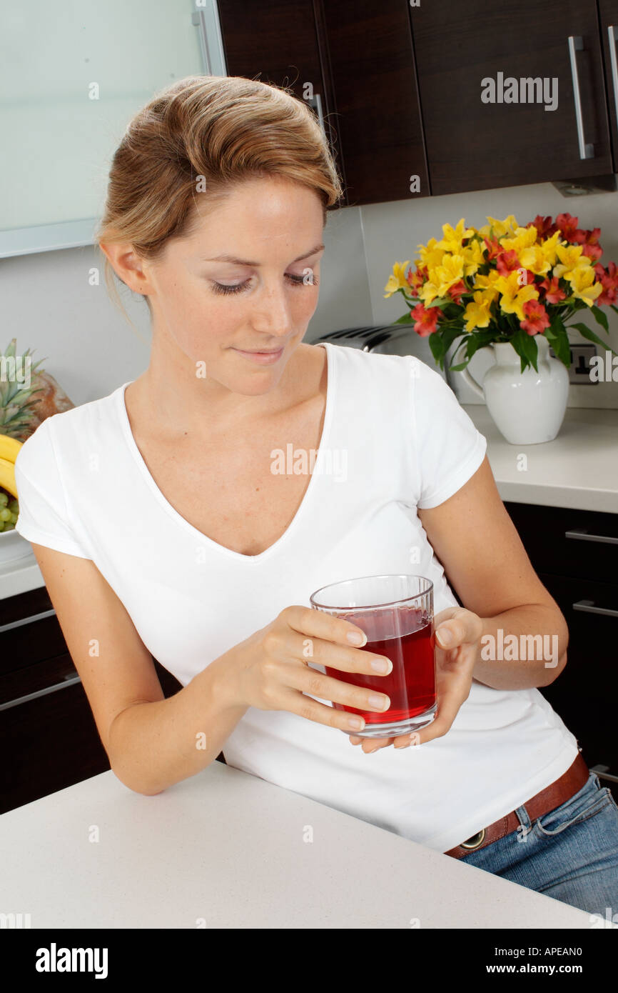 La donna in cucina a bere un bicchiere di succo di mirtillo palustre Foto Stock