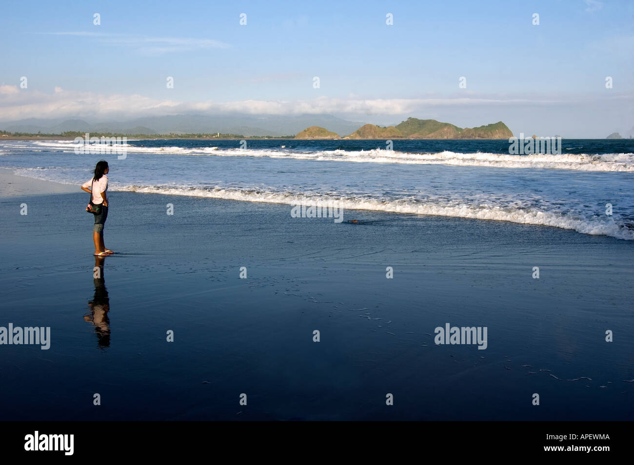 Un solitario donna indonesiana contemplando il mare da una sabbia scura beach in Java Orientale, Indonesia. Foto Stock