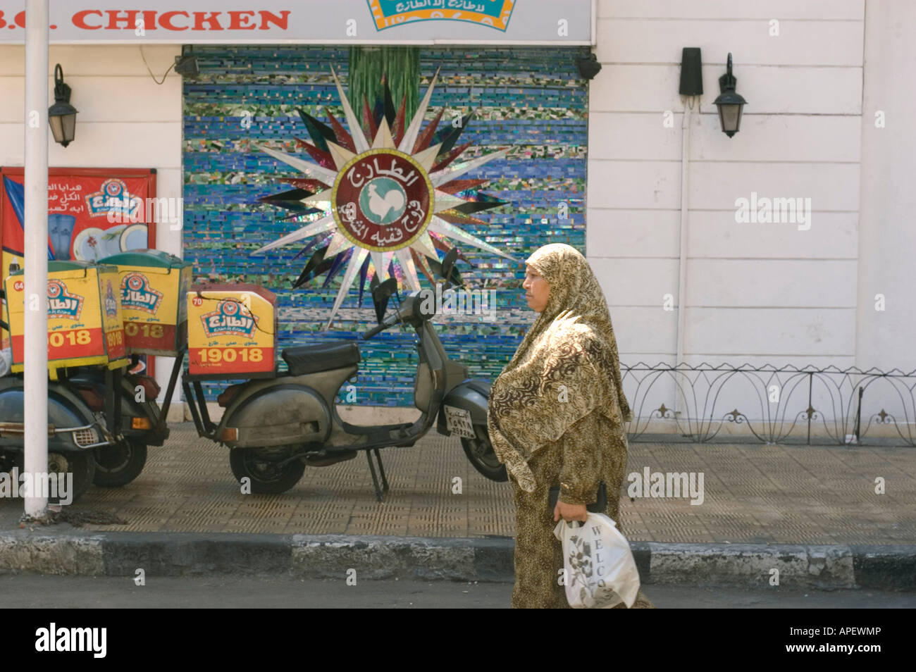 Donna con la copertura del capo e shopping bag passeggiate su Alessandria d Egitto Street di fronte a un ristorante fast food Foto Stock