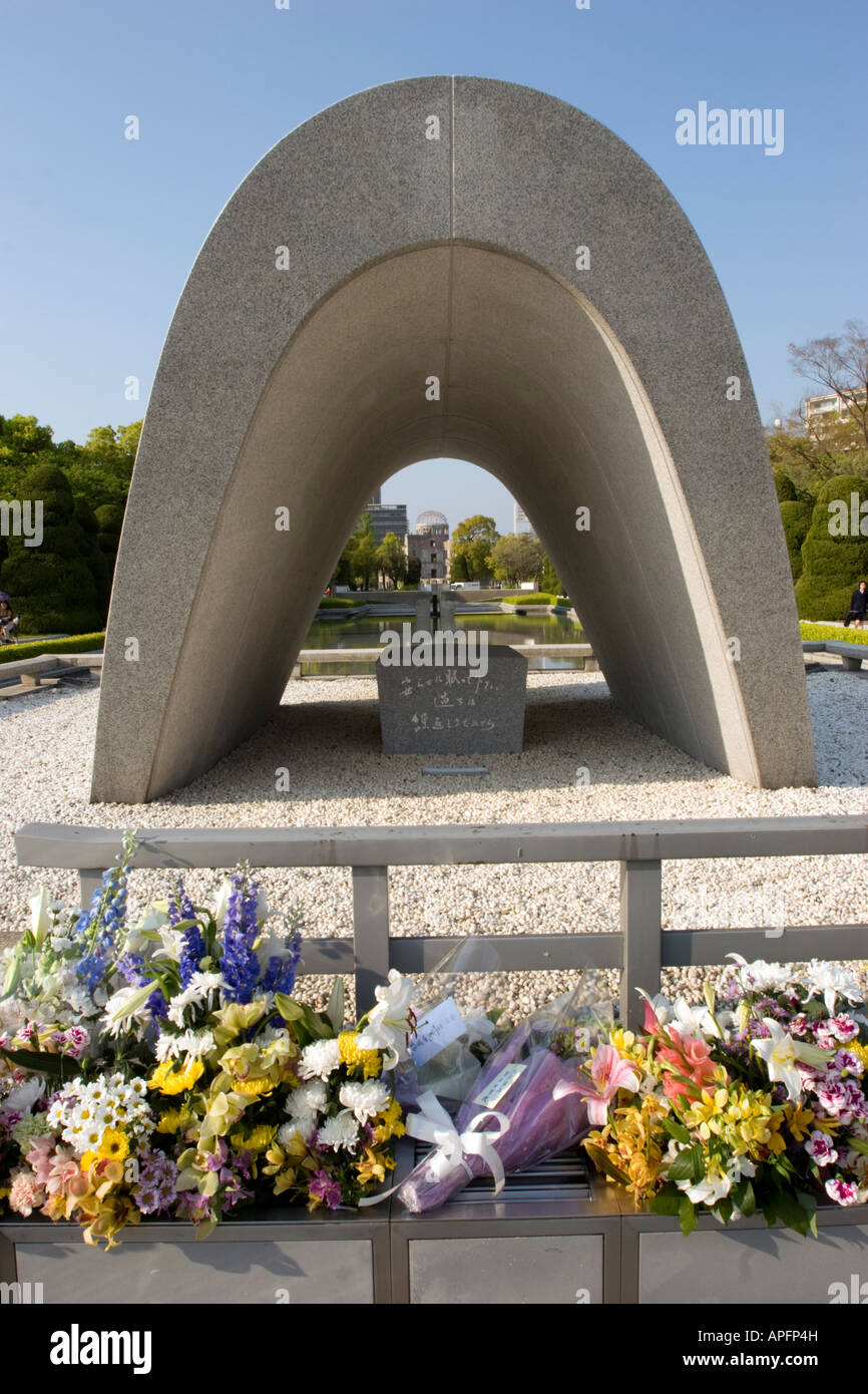 Fiori sotto il Cenotafio una bomba Memorial e la fiamma di pace con una vista su una cupola della bomba a Hiroshima il Giappone Foto Stock