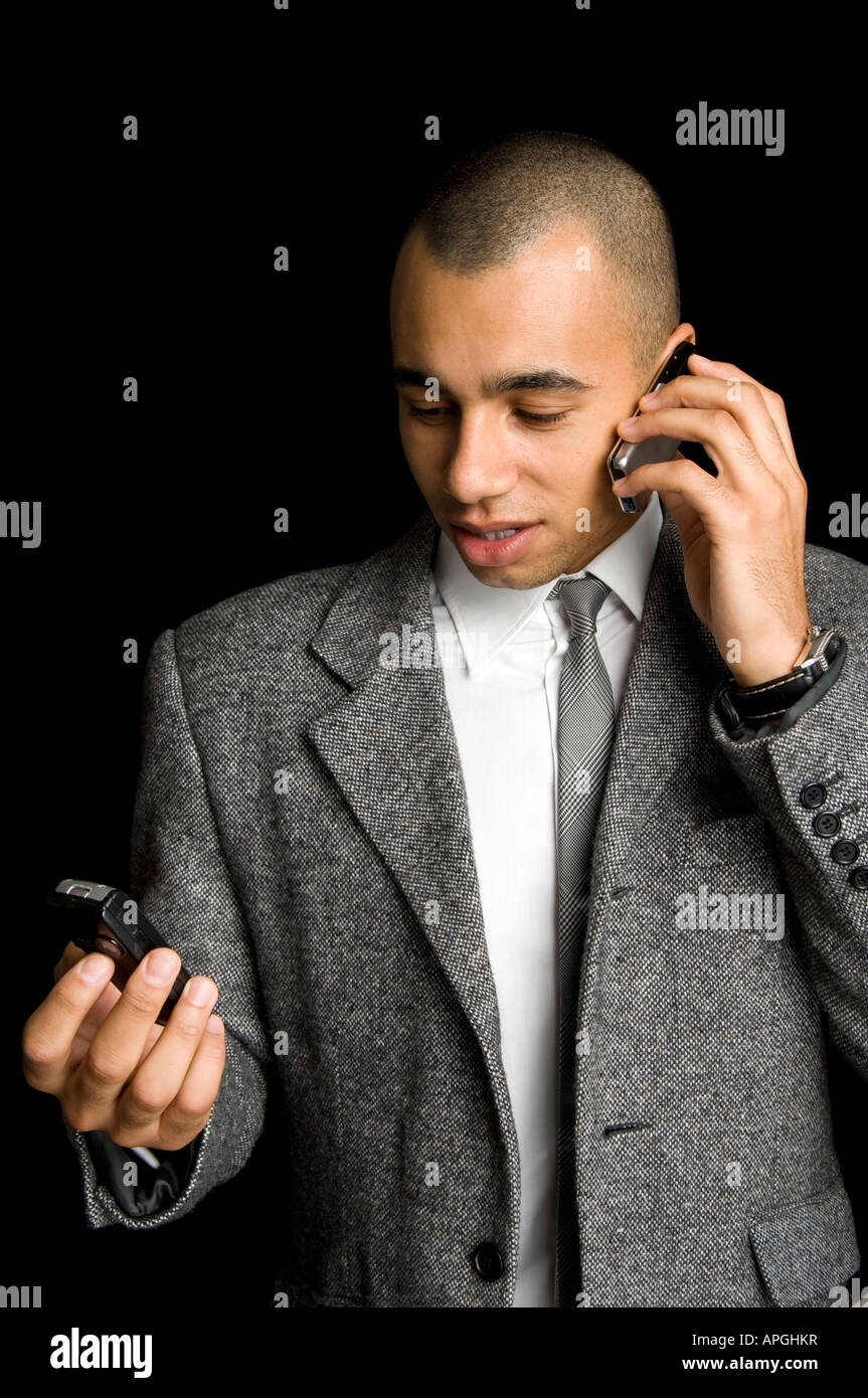Giovani razza mista imprenditore chattare su due telefoni cellulari Foto Stock