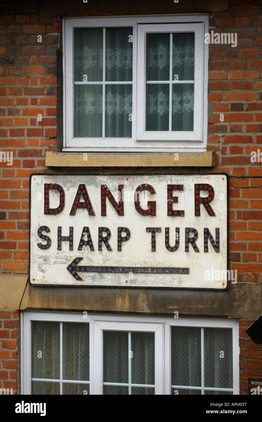 Una casa protetta su una curva stretta da un grande segno che legge 'curva tagliente del pericolo'. Foto di Jim Holden Foto Stock