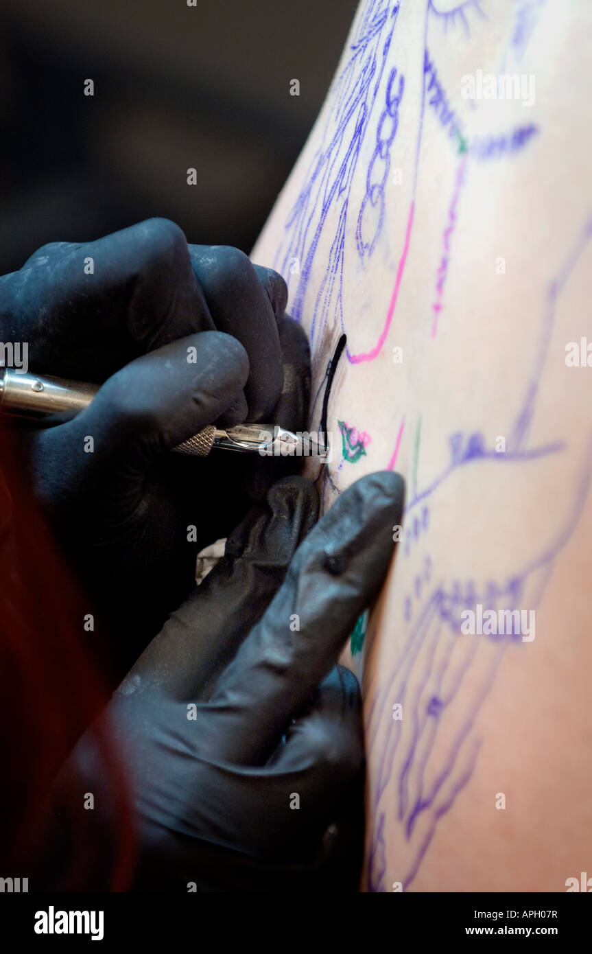 Un tatuaggio artista al lavoro di verniciatura di un disegno su un uomo con la schiena. Foto da Jim Holden. Foto Stock