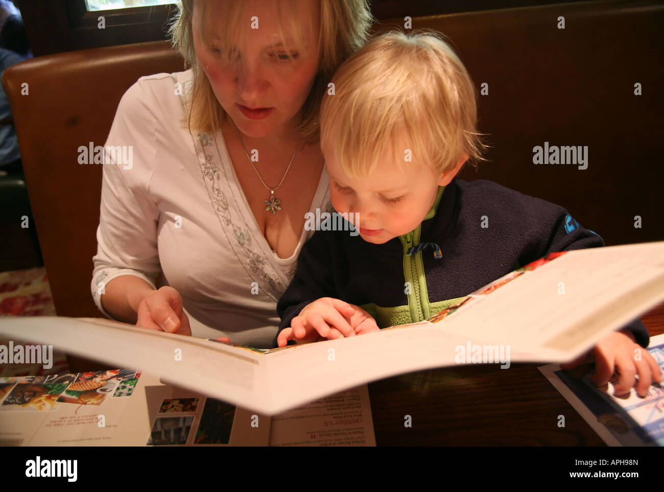 Madre aiutare i giovani ad un ragazzo a scegliere pasto dal menu di un ristorante Foto Stock