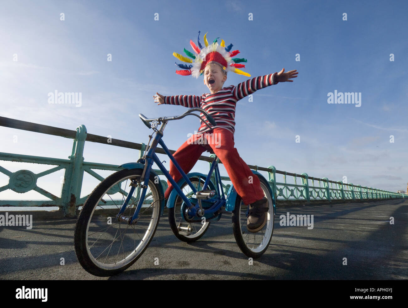 Un piccolo ragazzo in un rosso copricapo indiano urlando come suona su un trike sulla pista ciclabile sul lungomare di Brighton Foto Stock