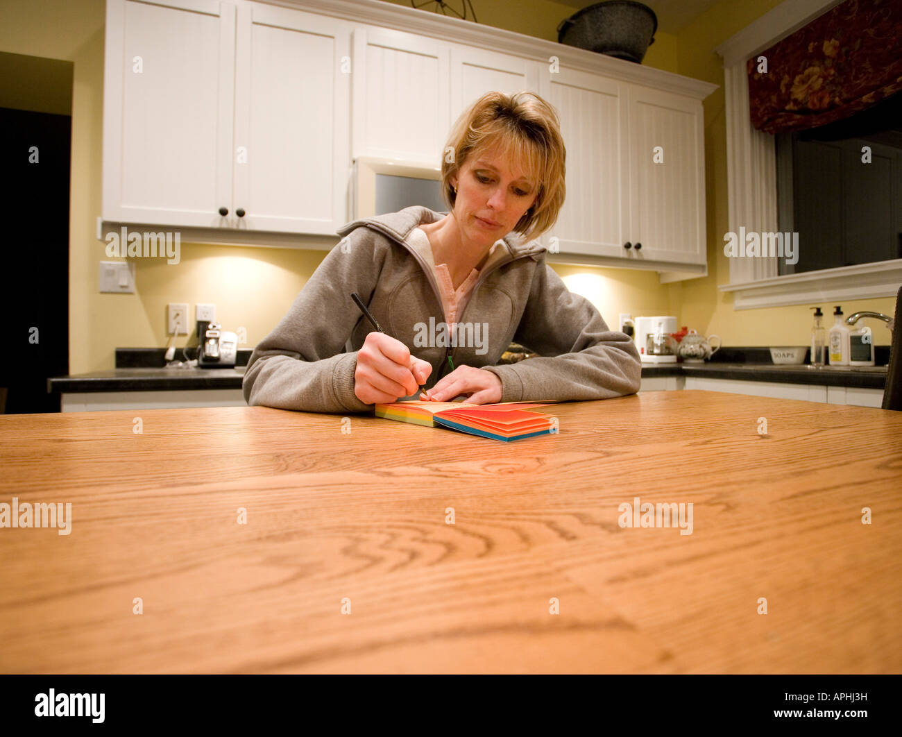 Donna iscritto [lista della spesa] al tavolo della cucina Foto Stock