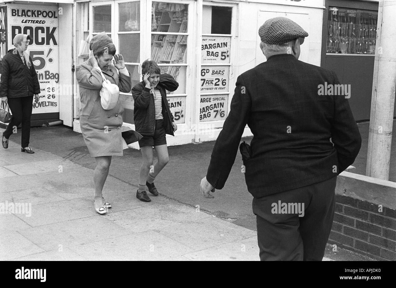 Madre e figlio soffiati dal vento forte, uomo anziano con un berretto di stoffa che cammina lungo il Golden Mile, Blackpool Lancashire Inghilterra 1970. 1970 UK HOMER SYKES Foto Stock