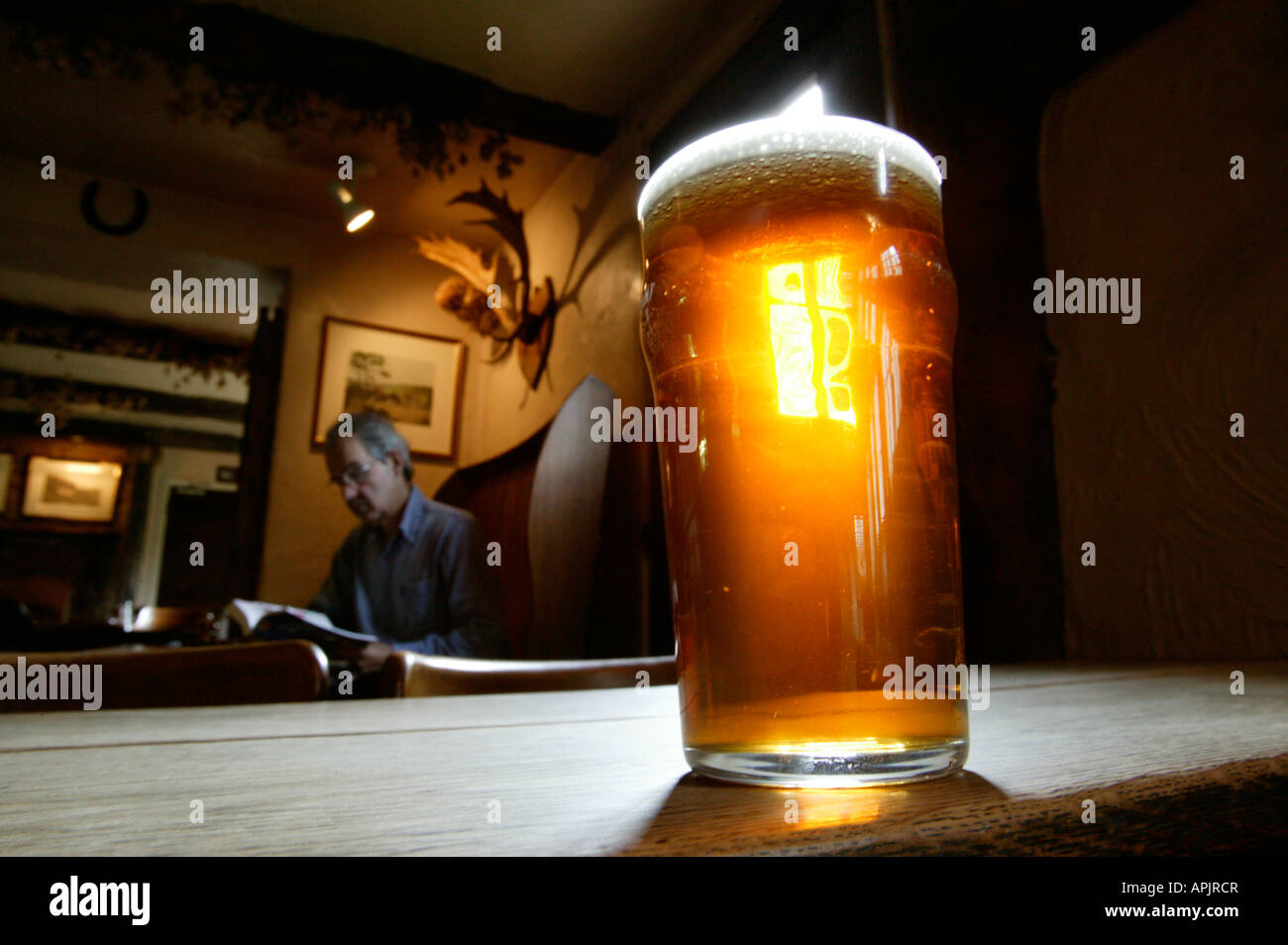 Una pinta di bitter in piedi su un vecchio tavolo di legno in un pub Inglese. Un uomo è seduta al tavolo dietro. Foto Stock