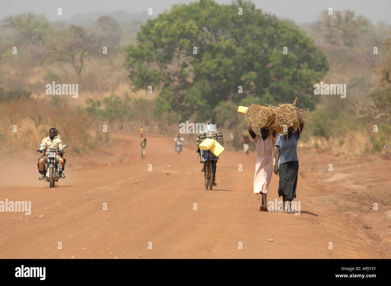 Due donne che trasportano materiali ricoprendo di paglia su una strada polverosa nel Sudan meridionale Foto Stock