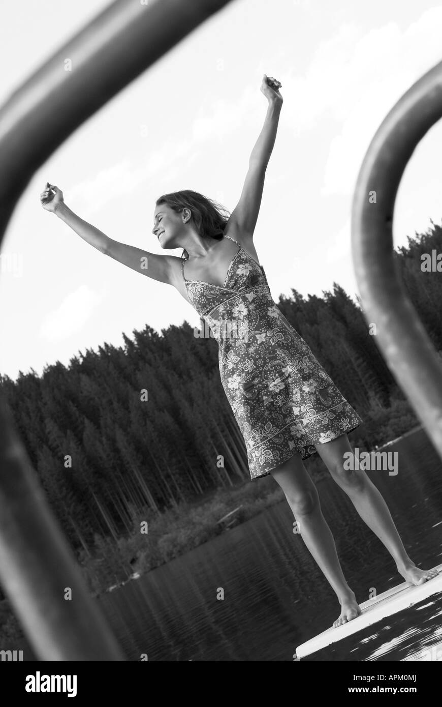 Giovane donna con abiti estivi stretching su una Springboard su un lago balneabile, godendo dell'estate, Austria, Erlaufsee Foto Stock