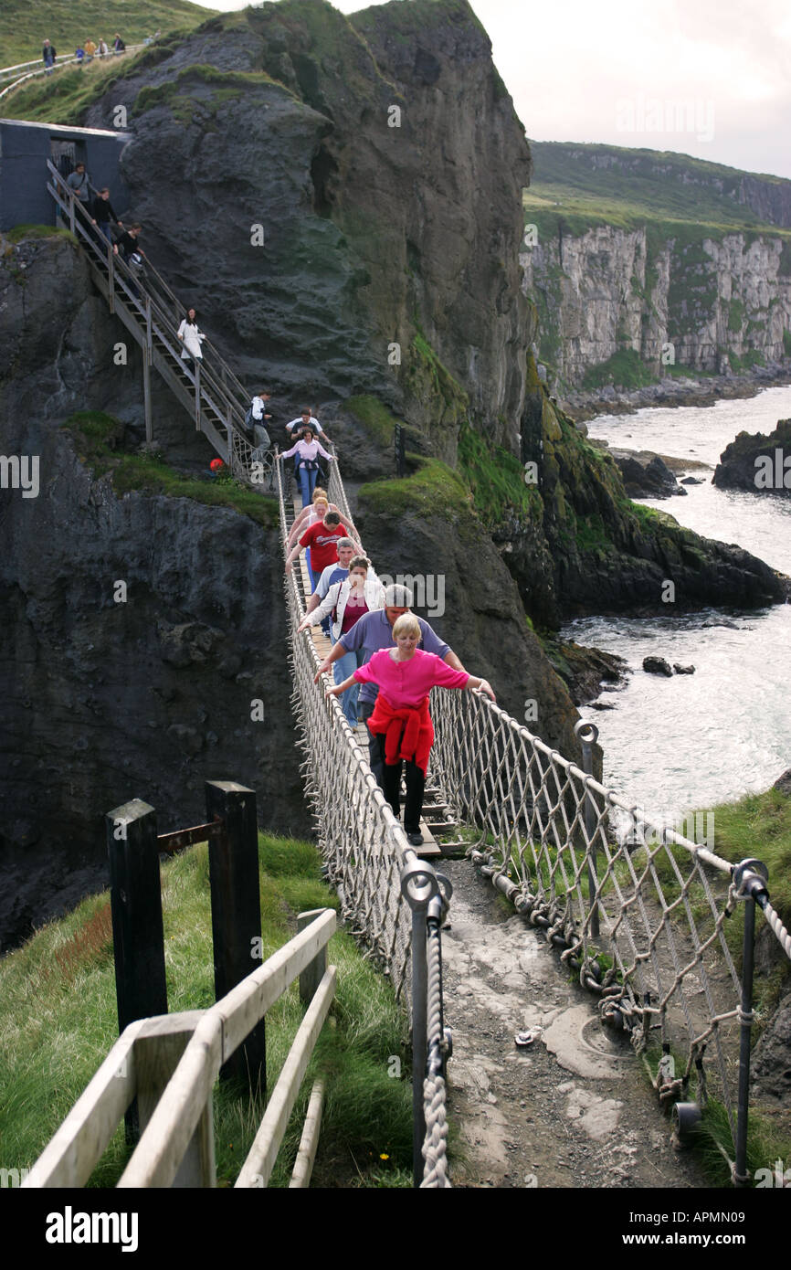I turisti attraversano il ponte di corda Carrick-a-Rede, un ponte sospeso  sulla costa di Antrim, nell'Irlanda del Nord, Regno Unito Foto stock - Alamy