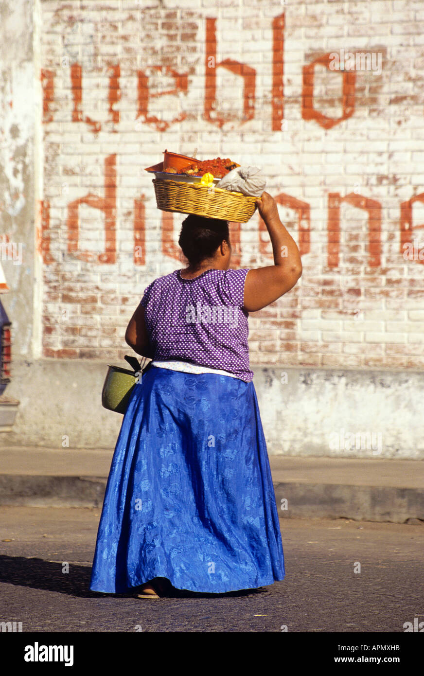 Un paffuto local donna vestita di un lungo mantello riuniti oscilla graziosamente con un paniere bilanciato sulla sua testa verso il mercato della città di Tehuantepec Foto Stock