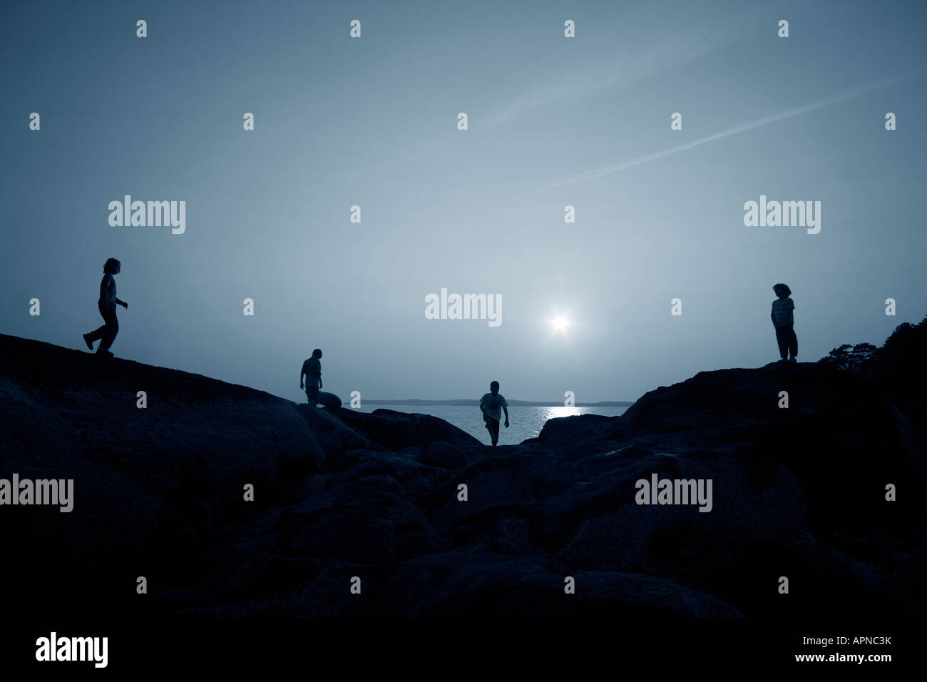 Silhouette di quattro ragazzi rocce di arrampicata sull'oceano Foto Stock