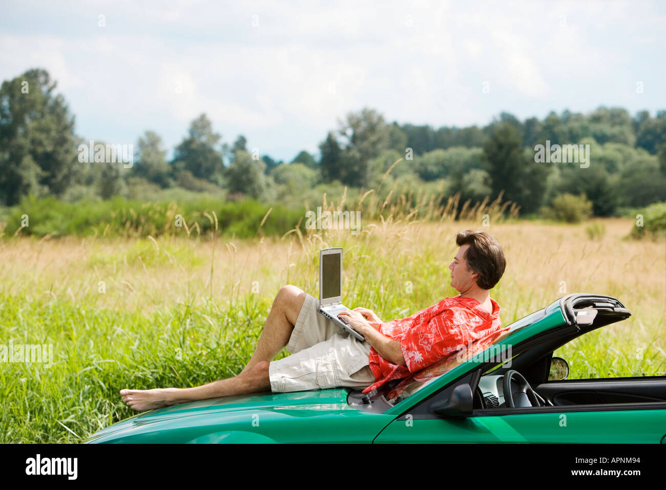 Uomo sulla vettura del cofano tramite computer portatile Foto Stock