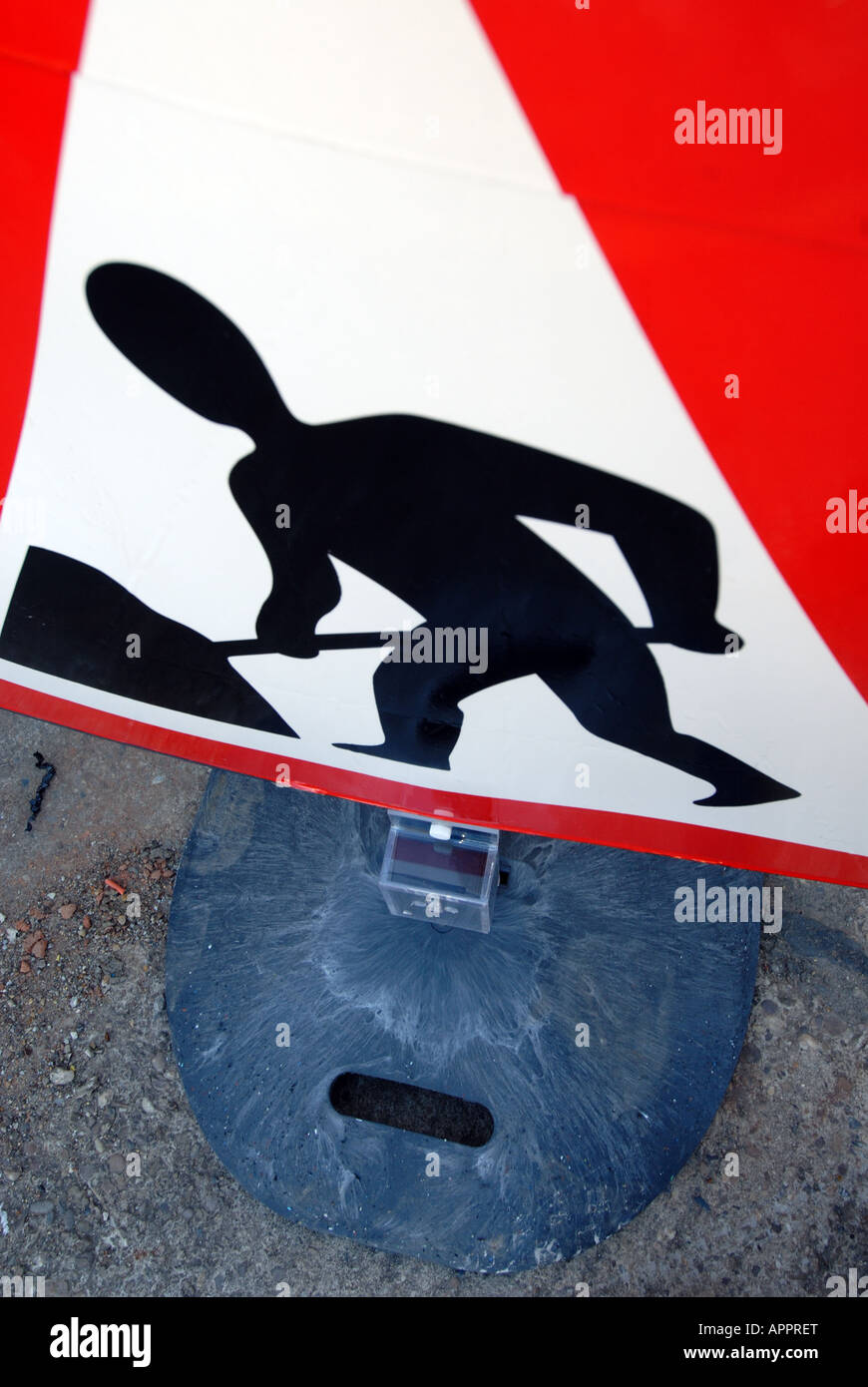 Guardando verso il basso vista ad alto livello di un uomo al lavoro roadworks firmare in bianco e rosso il triangolo di avvertenza che mostra uomini al lavoro in anticipo Foto Stock
