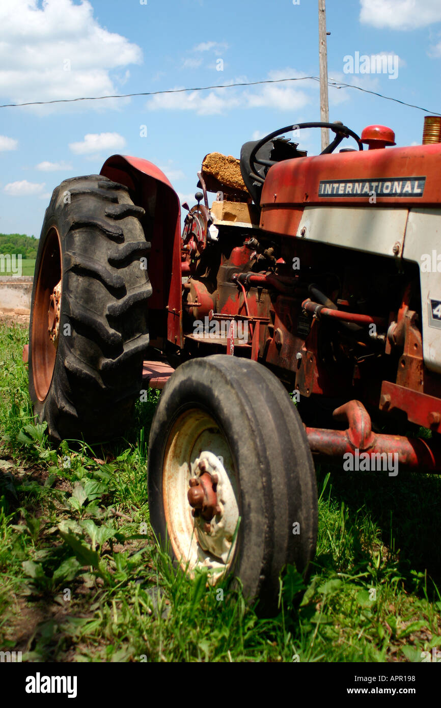 Il trattore farm raccolto nessun'altra attrezzatura zappa rurale erba verde blu cielo nuvole pneumatico rosso antico aratro antiquate John deer falciatrice Foto Stock