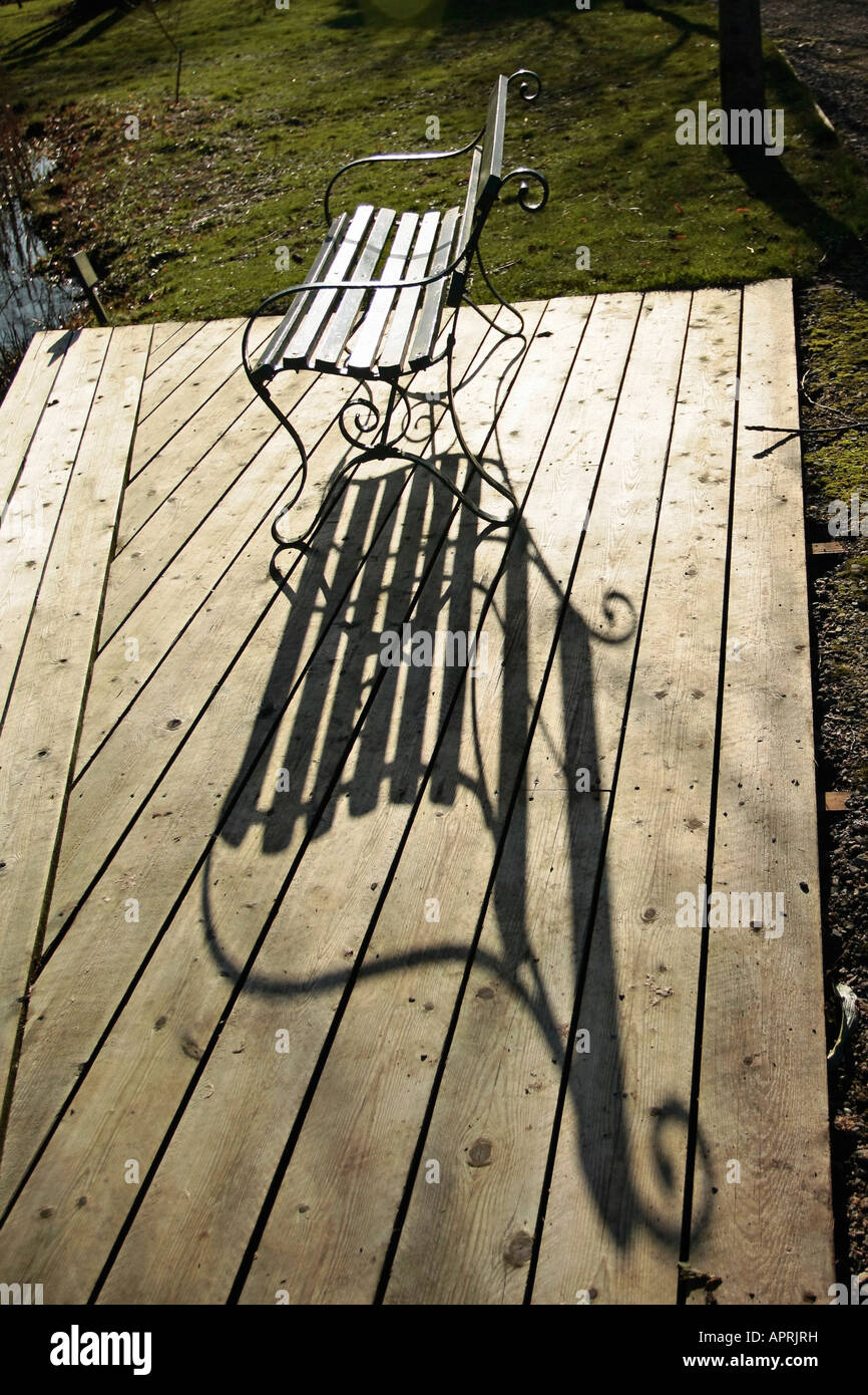 Posto in ferro battuto per il giardino che getta l'ombra su una pavimentazione in legno nel tardo inverno. Sussex, Inghilterra, Regno Unito Foto Stock