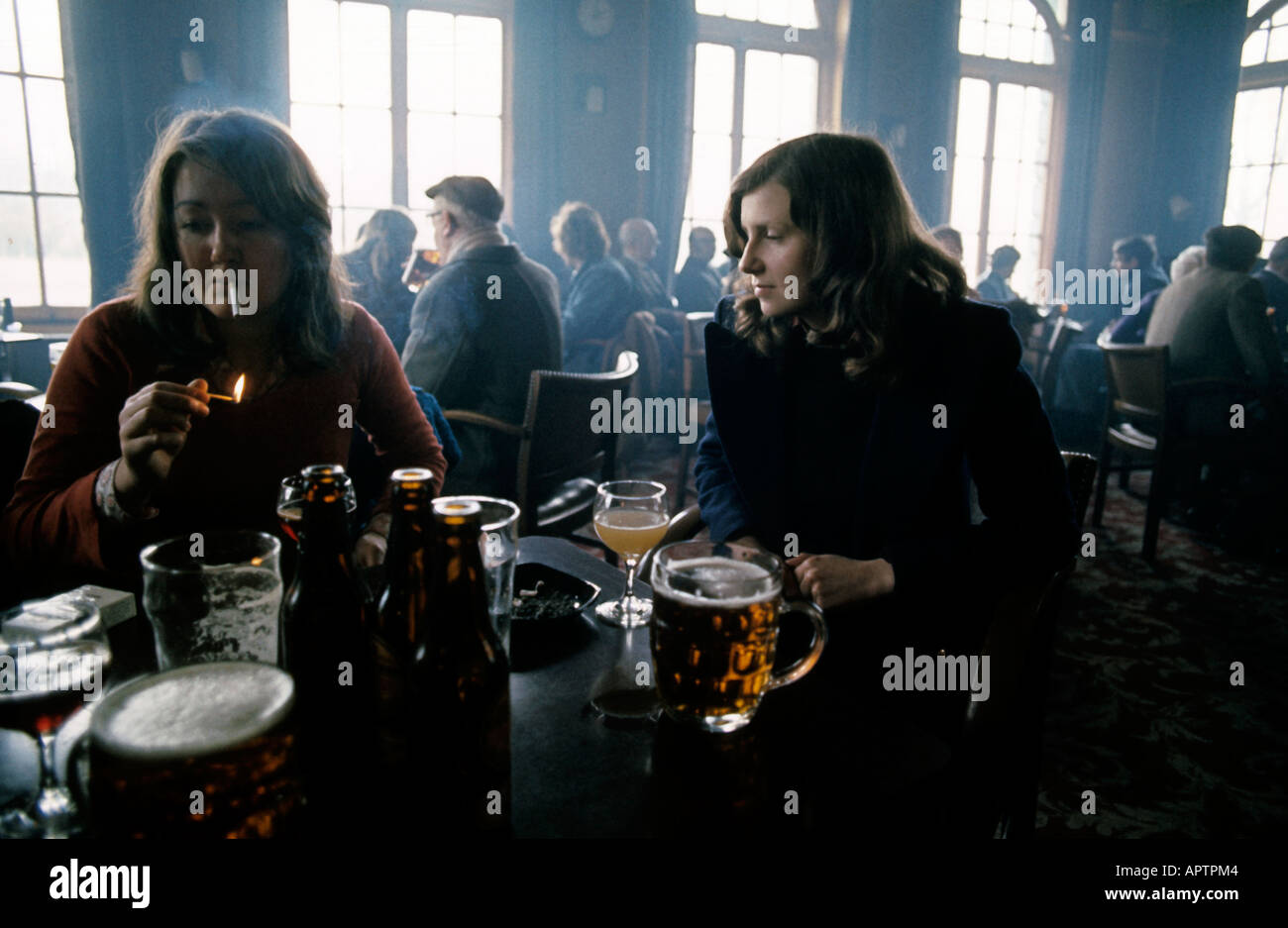 Persone in pub bar due femails wth pinte e corti sul tavolo una illuminazione di una sigaretta Foto Stock