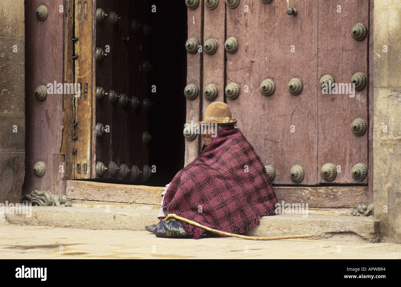 Vecchio mendicante femmina seduta prima del massiccio porte della Basilica di Nostra Signora di Copacabana vicino al lago Titicaca. Bolivia. Foto Stock