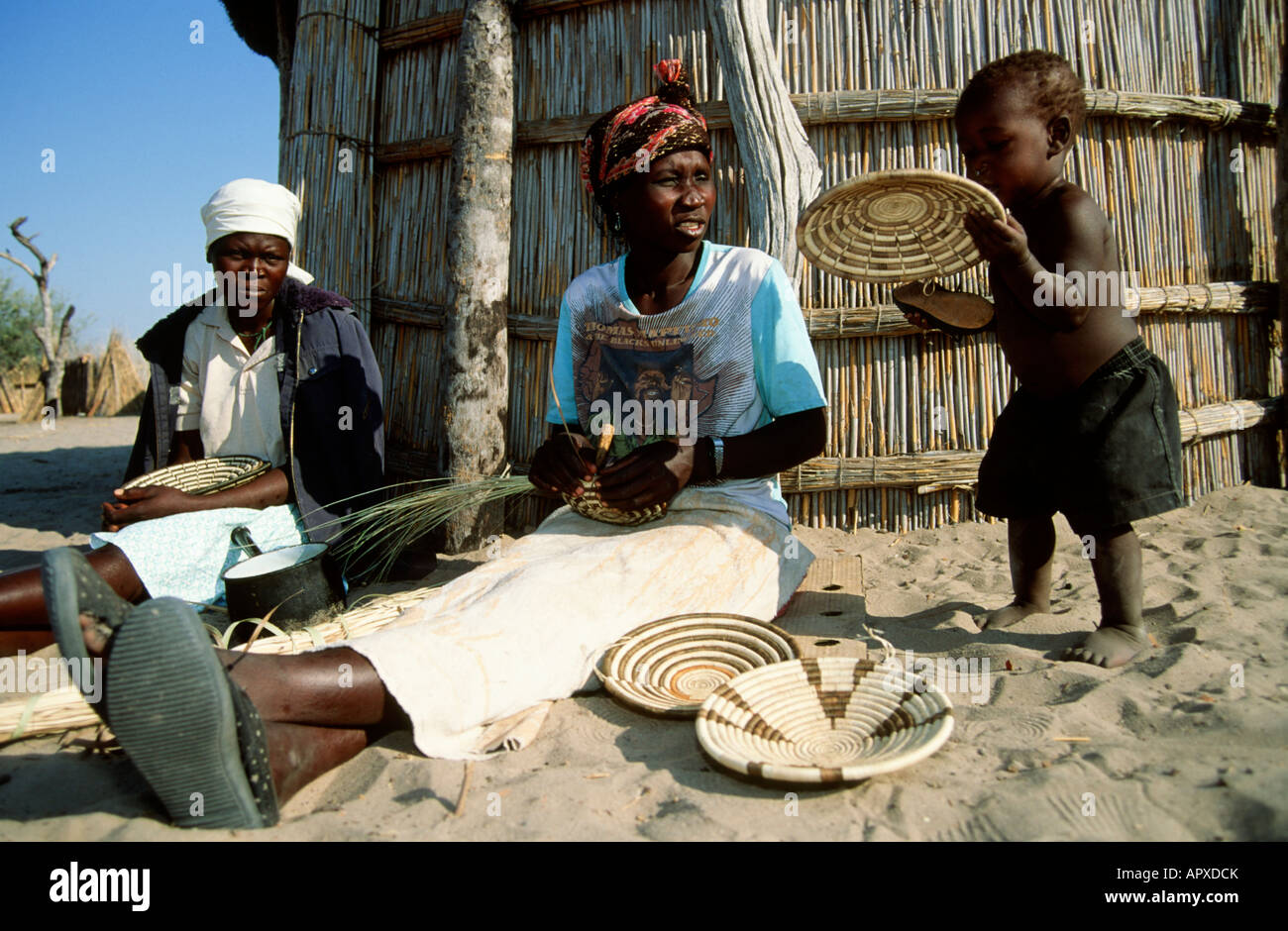 Donna tessitura di un tradizionale cestello del Botswana con un giovane bambino tenendo premuto uno dei cestelli Foto Stock