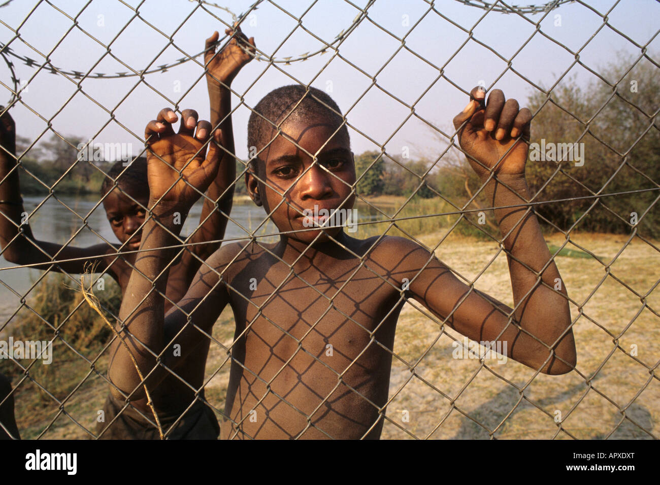 Due ragazzini appendere su di una recinzione perimetrale in un villaggio di Divundu Foto Stock
