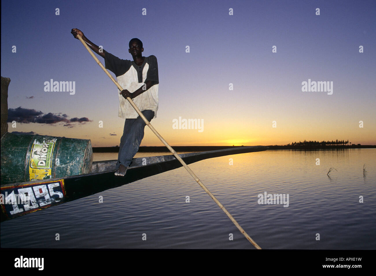 Un pilota pinasse (driver) dirige il suo mestiere home come il sole tramonta sul fiume Niger Foto Stock