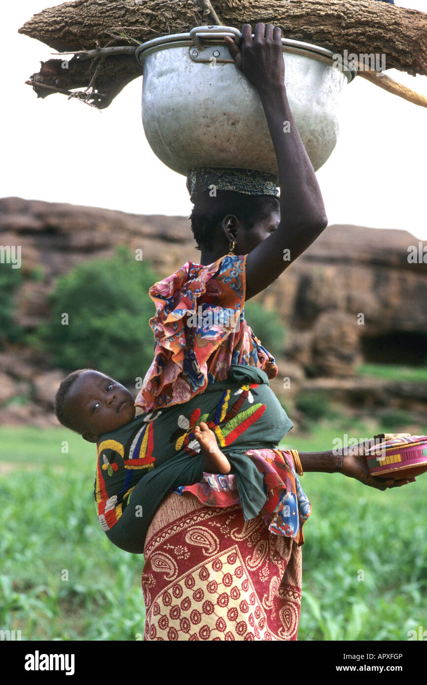 Giovane donna Peul con un bambino legato al suo indietro il bilanciamento di una pentola di metallo sul suo capo Foto Stock