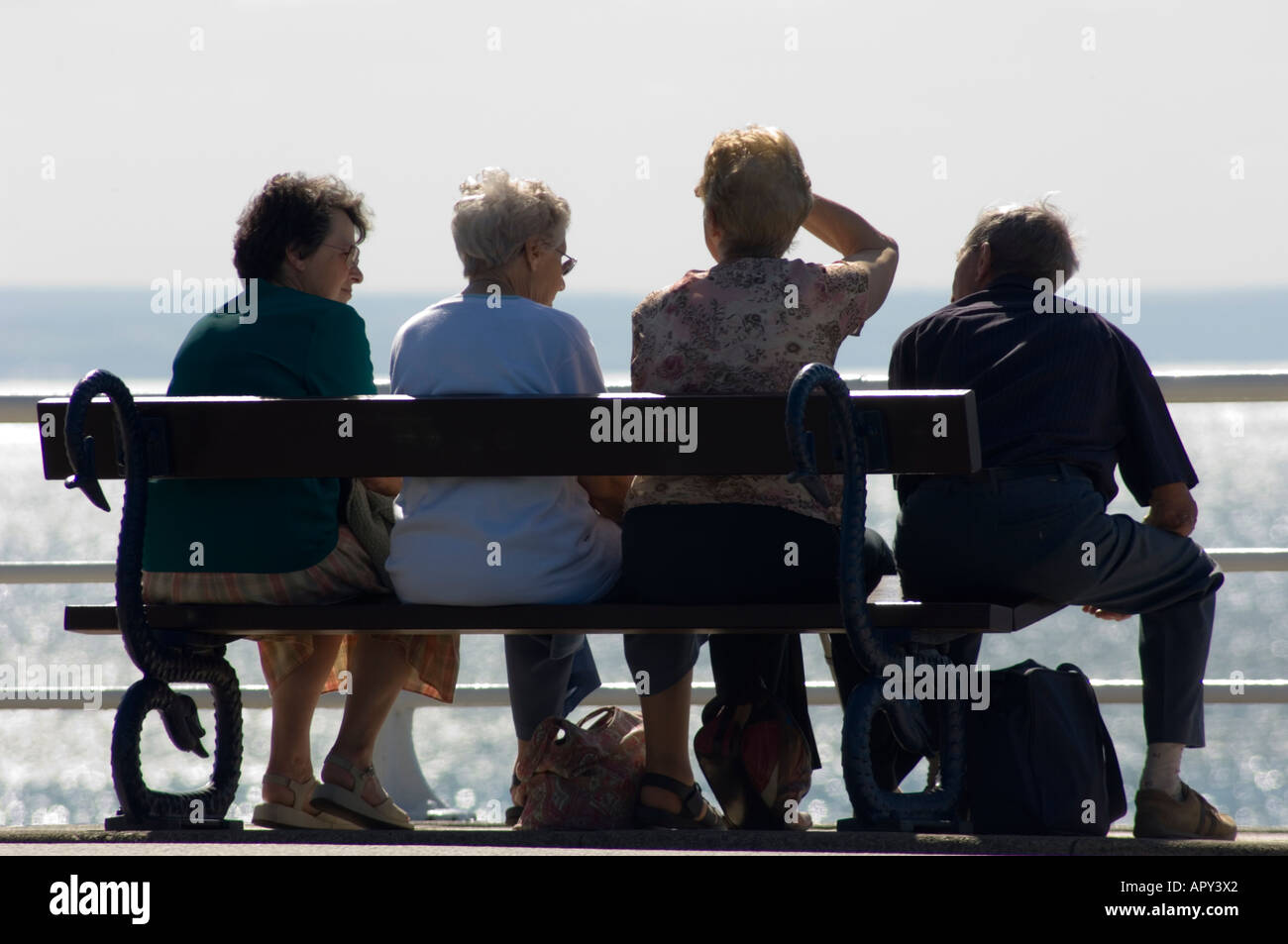 Vista posteriore di quattro persone di mezza età la gente seduta su una panchina Aberystwyth promenade guardando a Cardigan Bay, pomeriggio estivo REGNO UNITO Foto Stock