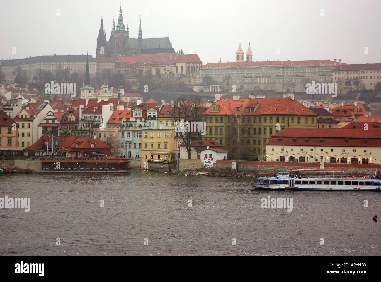 Vista dal ponte Carlo che mostra il fiume Moldava, una barca, edifici con tetti rossi e il Castello di Praga nella distanza. Foto Stock