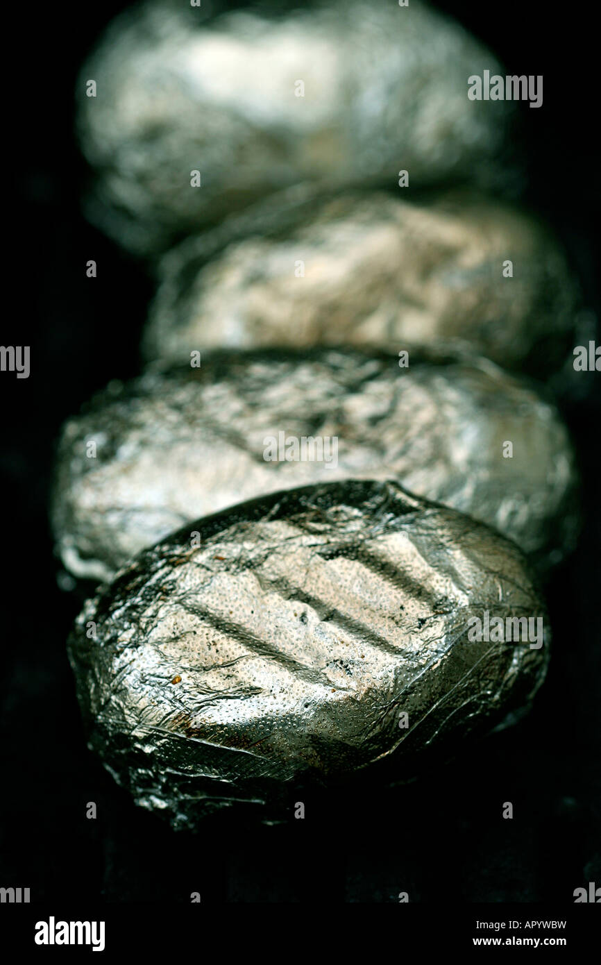 Patate avvolto in alluminio sfrigolante su barbecue Foto Stock