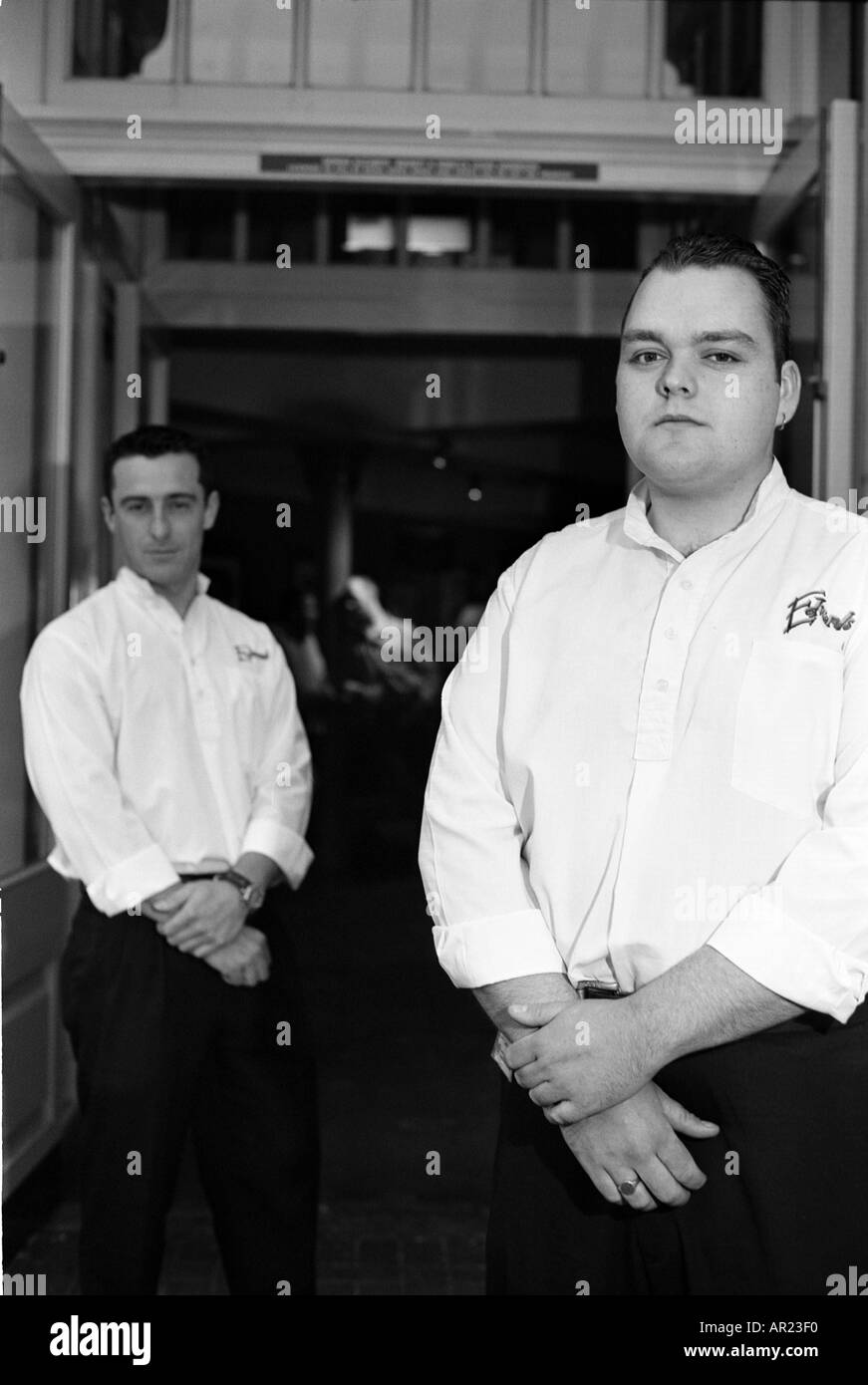 Due maschio portieri buttafuori al di fuori di un pub in bianco e nero monocromatico ingresso ritratti ritratto Foto Stock