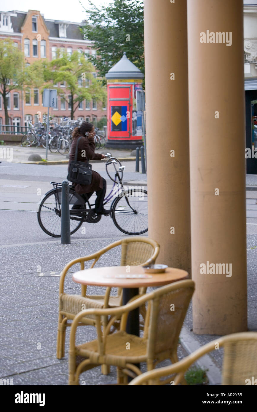 HOLLAND AMSTERDAM femmina nero ciclista OLTREPASSANDO CAFE e pilastri mentre parla con il suo telefono cellulare Foto Stock