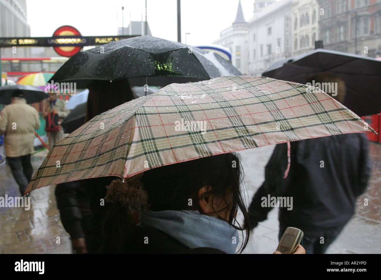Una donna controlla il suo telefono mobile con ombrello durante una pioggia pesante di pioggia, Tottenham Court Road, Londra, Regno Unito. Foto Stock