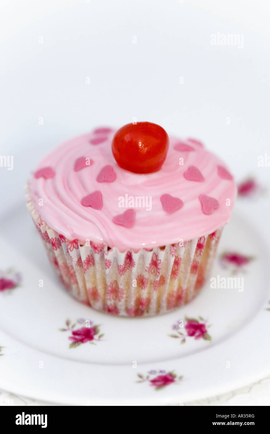 Home cotta Cup cake o torta di fata. Pan di Spagna con Rosa ghiaccio fondente e una ciliegia sulla parte superiore - servita su un vintage cina piastra. Foto Stock
