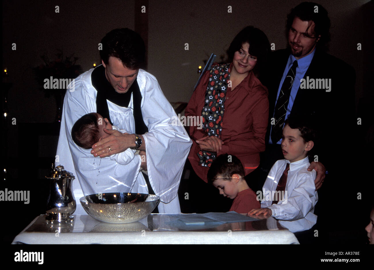 Battesimo cristiano con sacerdote che bagna la testa del bambino e la famiglia che guarda, Canada Foto Stock