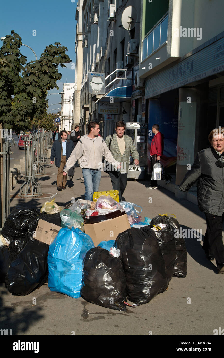 I pedoni a piedi attorno a Bin sacchetti di rifiuti oggetto di pratiche di dumping sul lato di una strada trafficata a Banja Luka, Bosnia Erzegovina Foto Stock