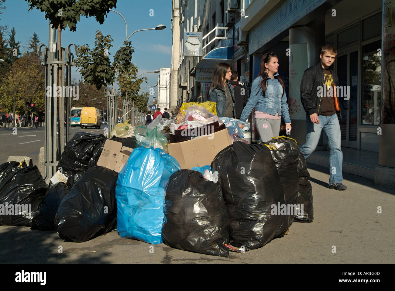 I pedoni a piedi attorno a Bin sacchetti di rifiuti oggetto di pratiche di dumping sul lato di una strada trafficata a Banja Luka, Bosnia Erzegovina Foto Stock