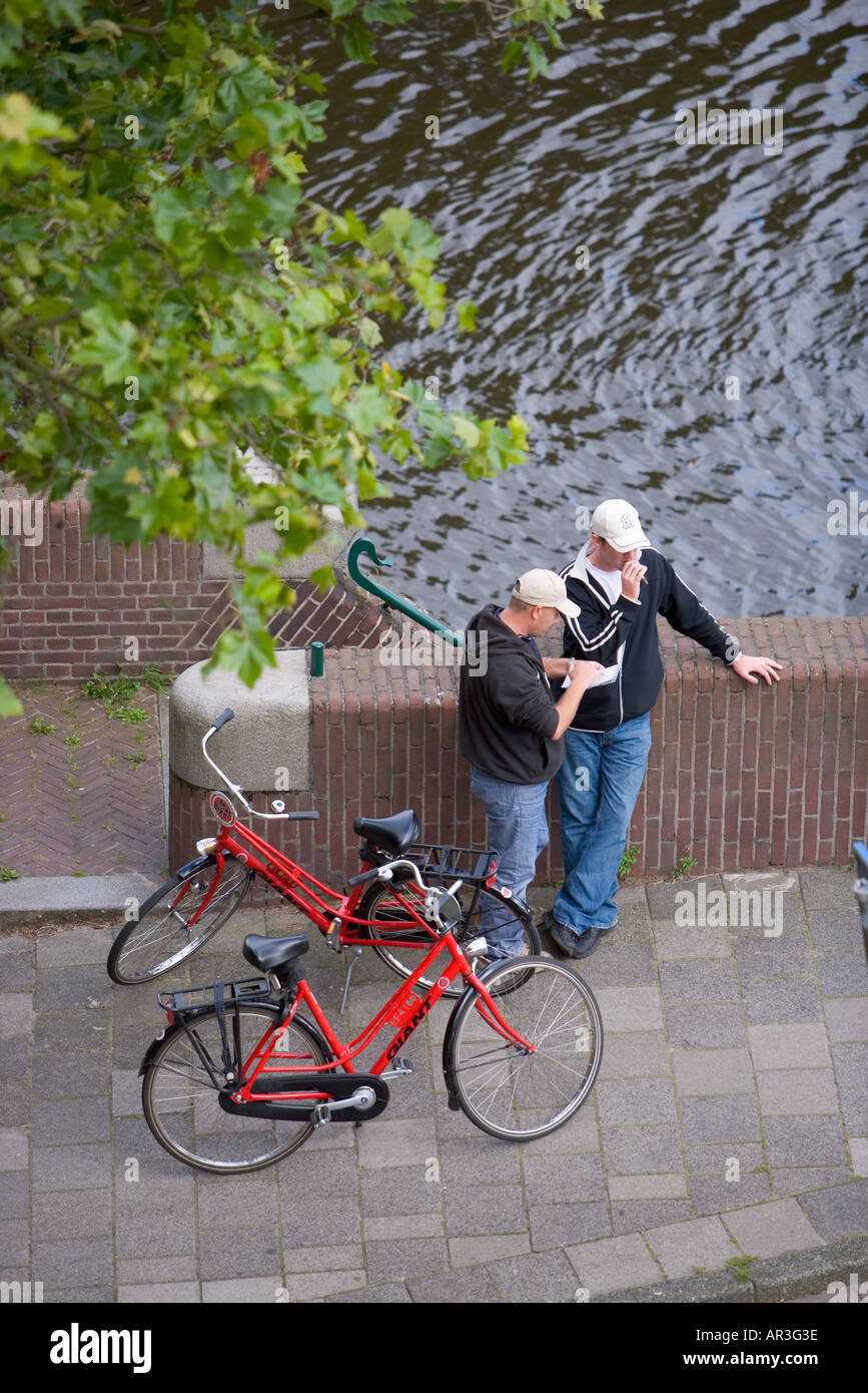 HOLLAND AMSTERDAM due uomini stavano in piedi accanto a loro bici rosso di fumare un giunto di cannabis e guardando una mappa Foto Stock
