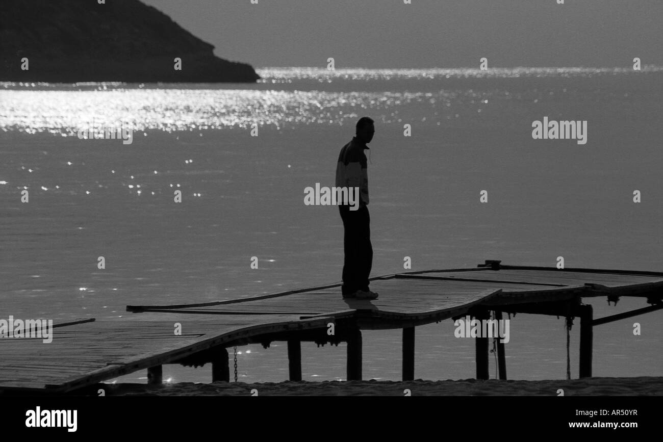 L'uomo stagliano in piedi su un molo con sole luminoso acceso mare sullo sfondo. Foto Stock