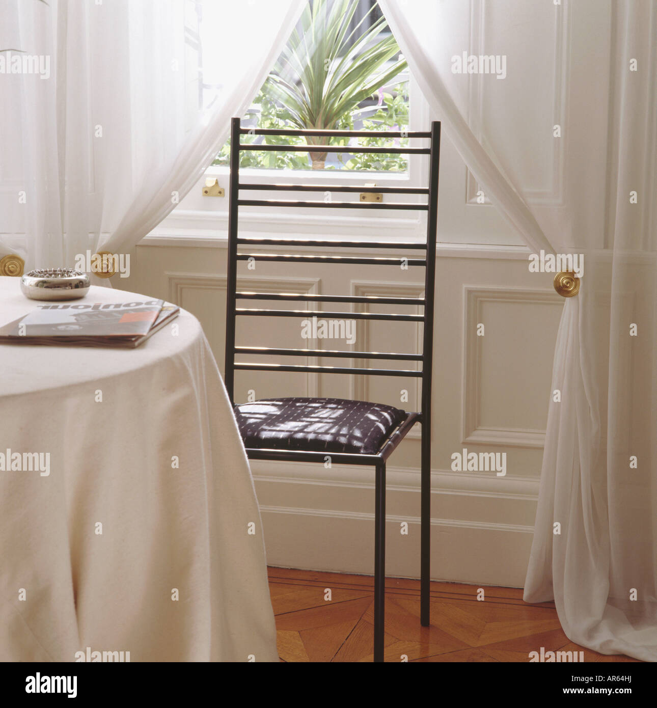 Nero Sedia in metallo nella parte anteriore della finestra con bianco tende di voile Foto Stock