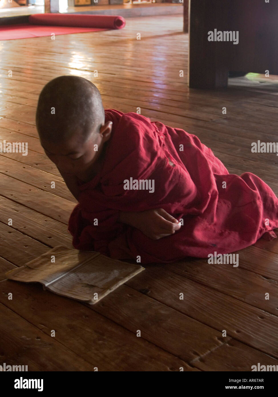 Giovane monaco lettura il suo monastero pavimento in Myanmar Foto Stock