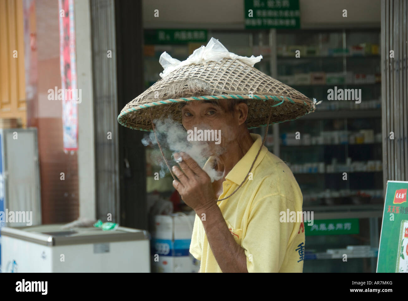 L'agricoltore cinese indossando un tradizionale ha sottolineato cappello di paglia di fumare in un mercato locale, Fuli village, Yangshuo. Foto Stock