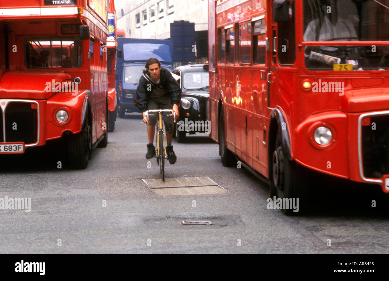 Ciclista senza casco attraverso il traffico di Londra Foto Stock