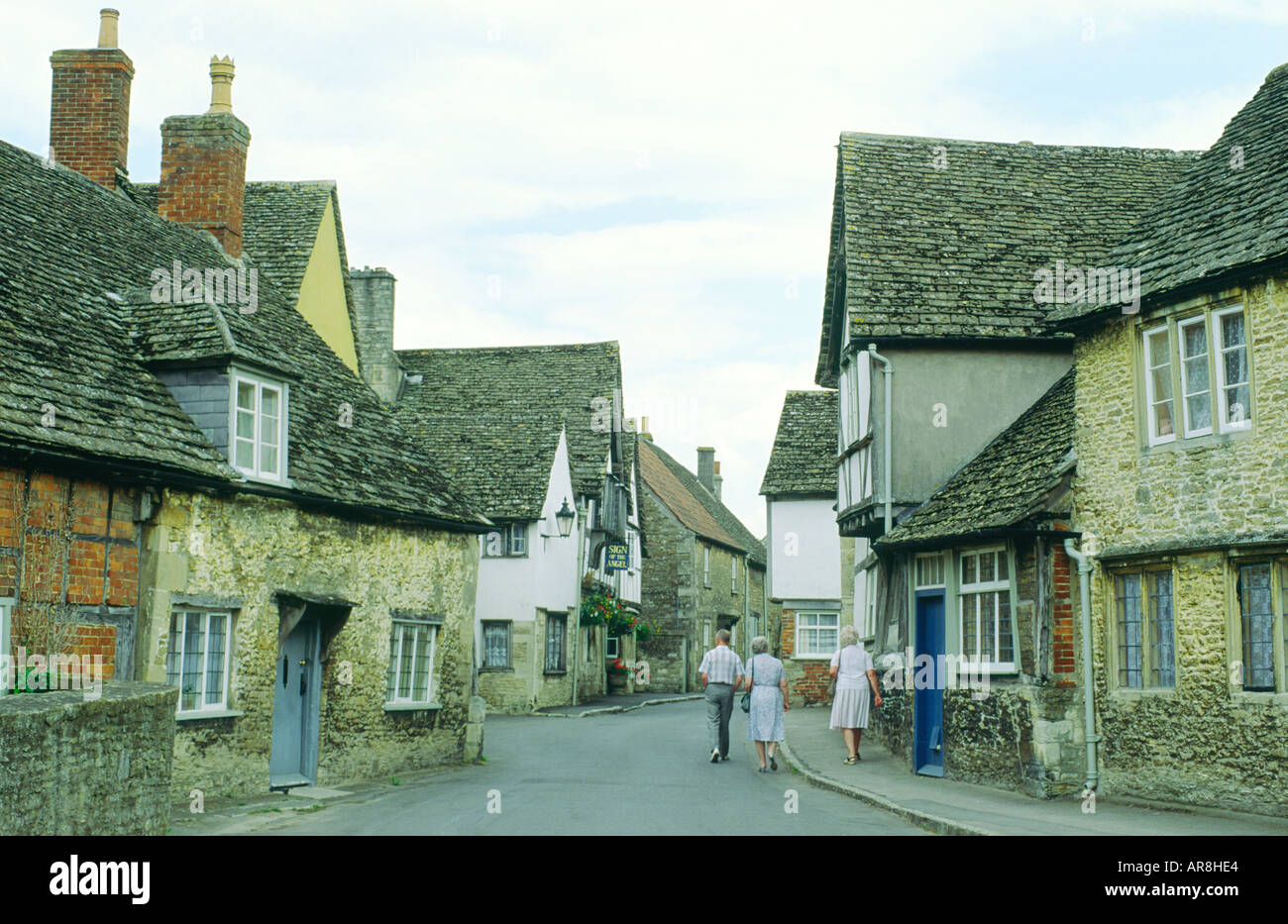 Lacock villaggio nel Wiltshire, Inghilterra. I visitatori a piedi verso il basso della strada di vecchie case verso casa pubblica denominata Segno dell'Angelo. Foto Stock