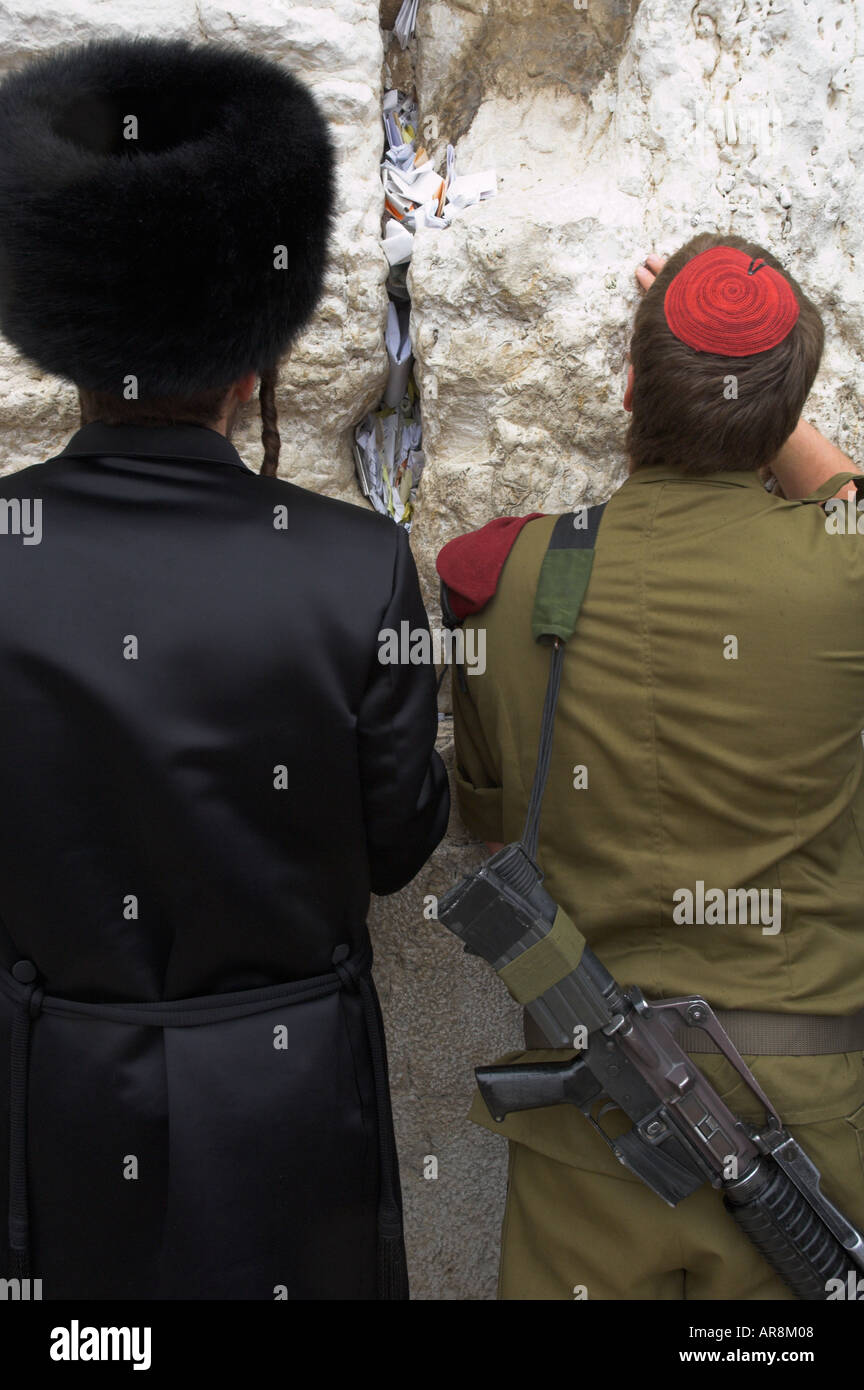 Israele Gerusalemme Muro Occidentale close up di un ebreo ortodosso in corrispondenza della parete pregando accanto a un soldato con la pistola in verticale Foto Stock