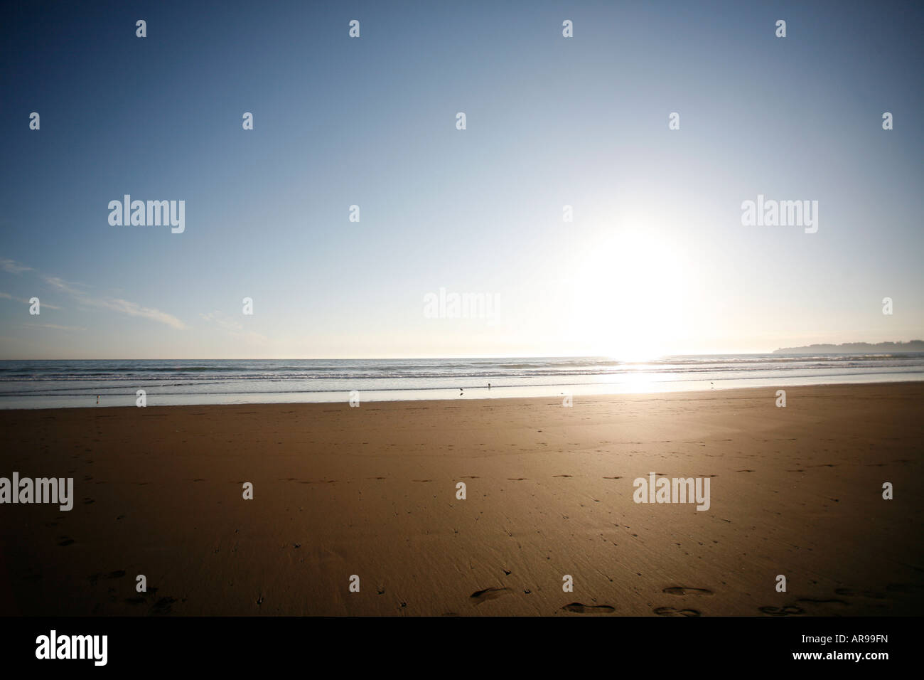 Guardando il mare dalla spiaggia come il sole tramonta oltre l'orizzonte Foto Stock