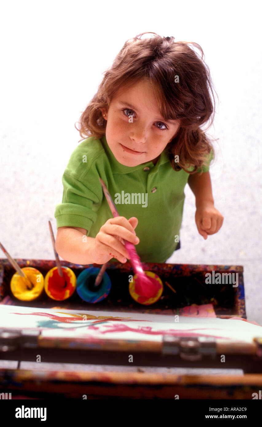 CLASSE D'ARTE, bambina di 4-6 anni con pennello presso il tradizionale cavalletto della scuola d'arte in legno in classe, si presenta felice determinata sorridente e sicura di sé Foto Stock