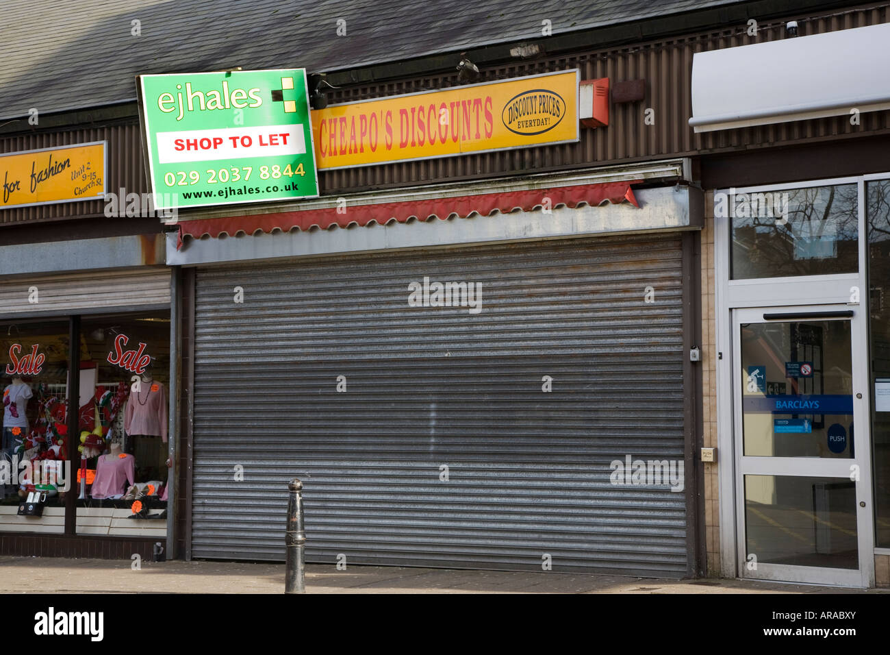 Negozio chiuso con ante e lasciare agente immobiliare segno nella principale strada dello shopping Abertillery Wales UK Foto Stock