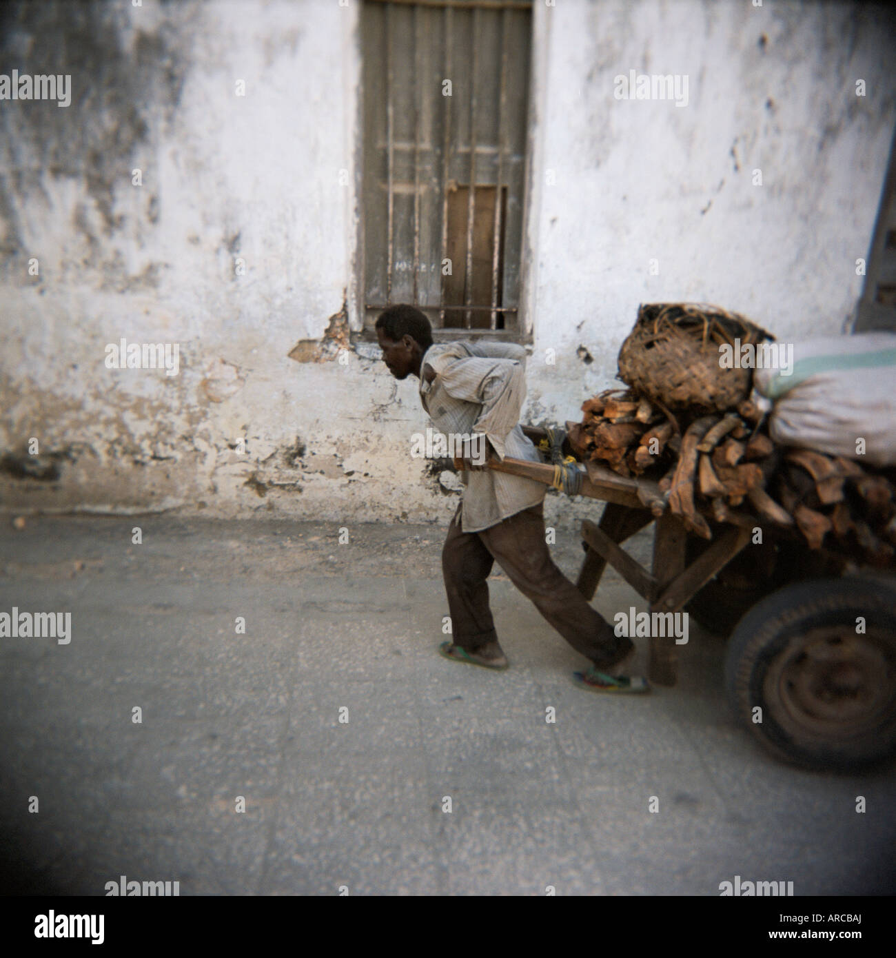 L'uomo tirando il carrello lungo la via stretta, Stone Town Zanzibar, Tanzania, Africa orientale, Africa Foto Stock