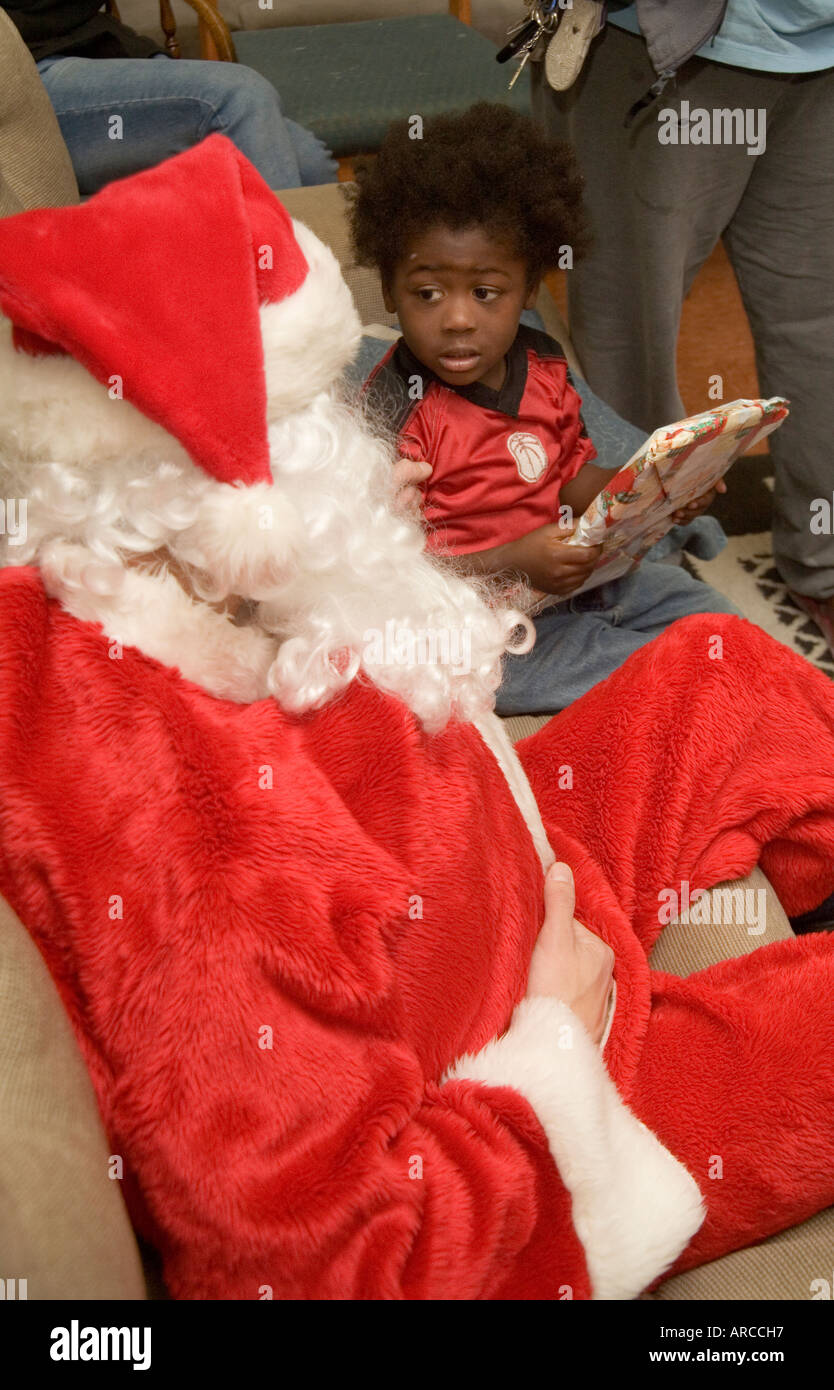 Un ragazzo spaventato è incoraggiato a visitare un Babbo Natale volontario durante le attività di Natale per le persone a basso reddito e i bambini senza tetto Foto Stock